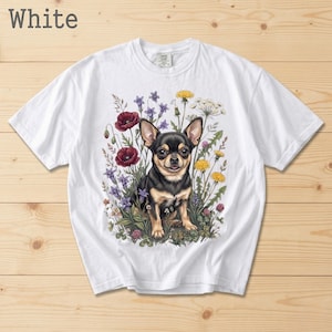 May include: White t-shirt featuring a detailed illustration of a black and tan Chihuahua dog surrounded by colorful wildflowers. The text "White" is printed at the top left. The shirt is made of a soft, comfortable material.