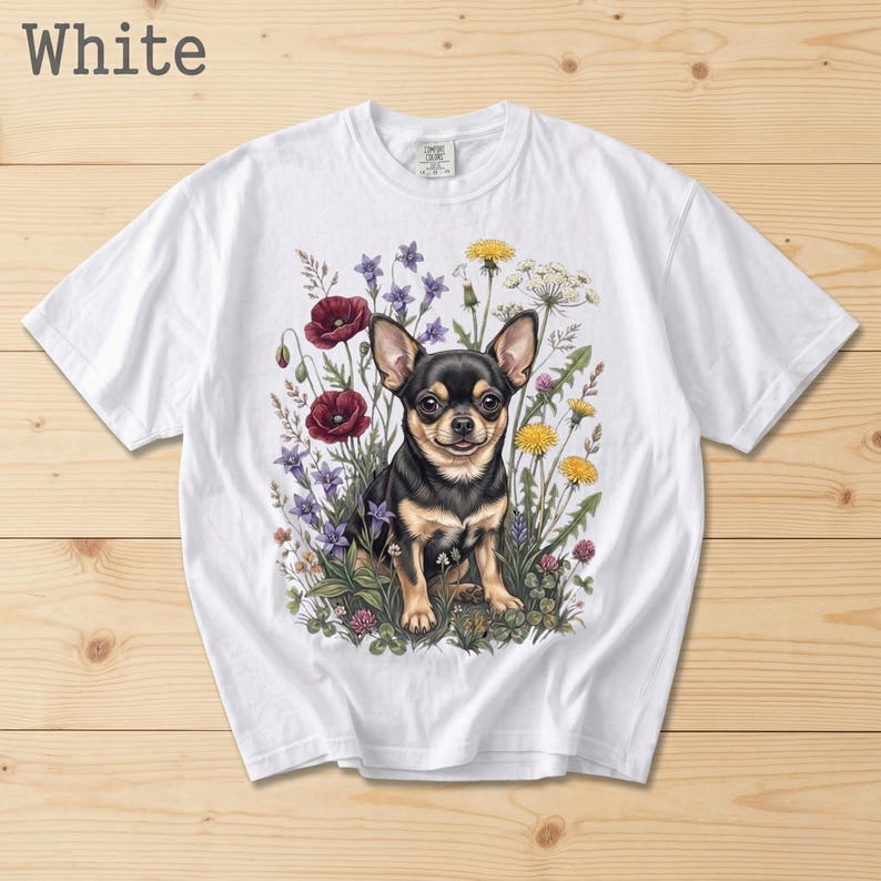 May include: White t-shirt featuring a detailed illustration of a black and tan Chihuahua dog surrounded by colorful wildflowers. The text "White" is printed at the top left. The shirt is made of a soft, comfortable material.