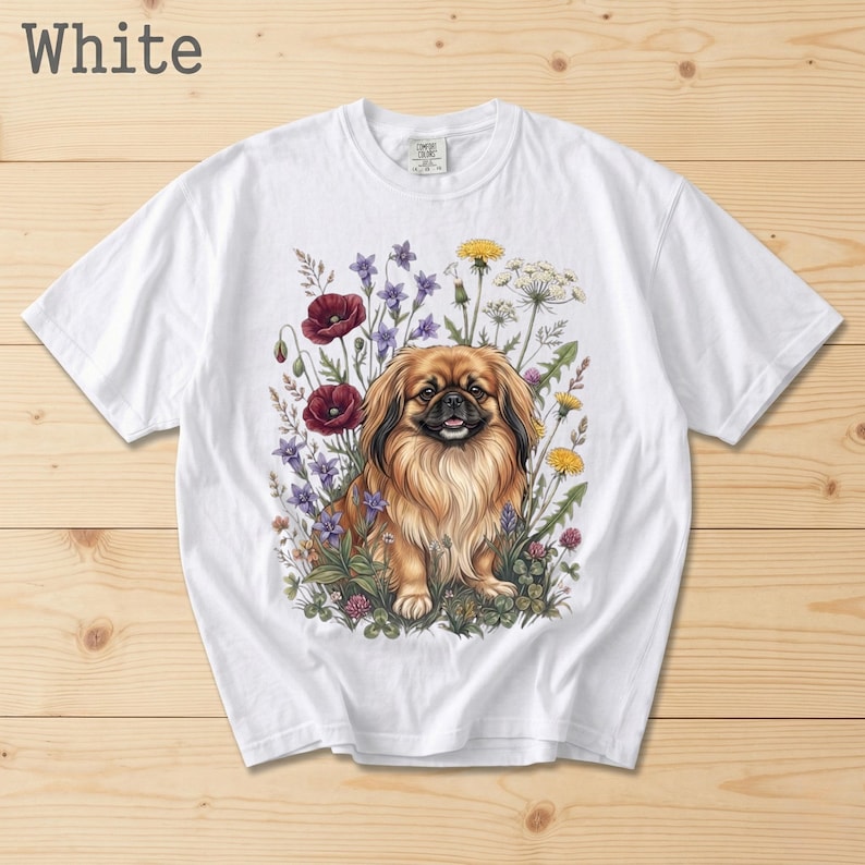 May include: White t-shirt featuring a detailed illustration of a Pekingese dog surrounded by colorful wildflowers. The dog has brown and tan fur, and the flowers include red poppies, purple blooms, and yellow dandelions. The word "White" is printed at the top.