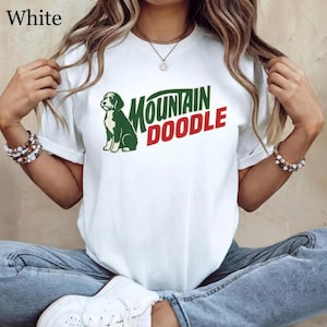 May include: White t-shirt with a green and red graphic that reads "MOUNTAIN DOODLE" and a green doodle dog illustration. The word "White" is in the top left corner of the shirt.
