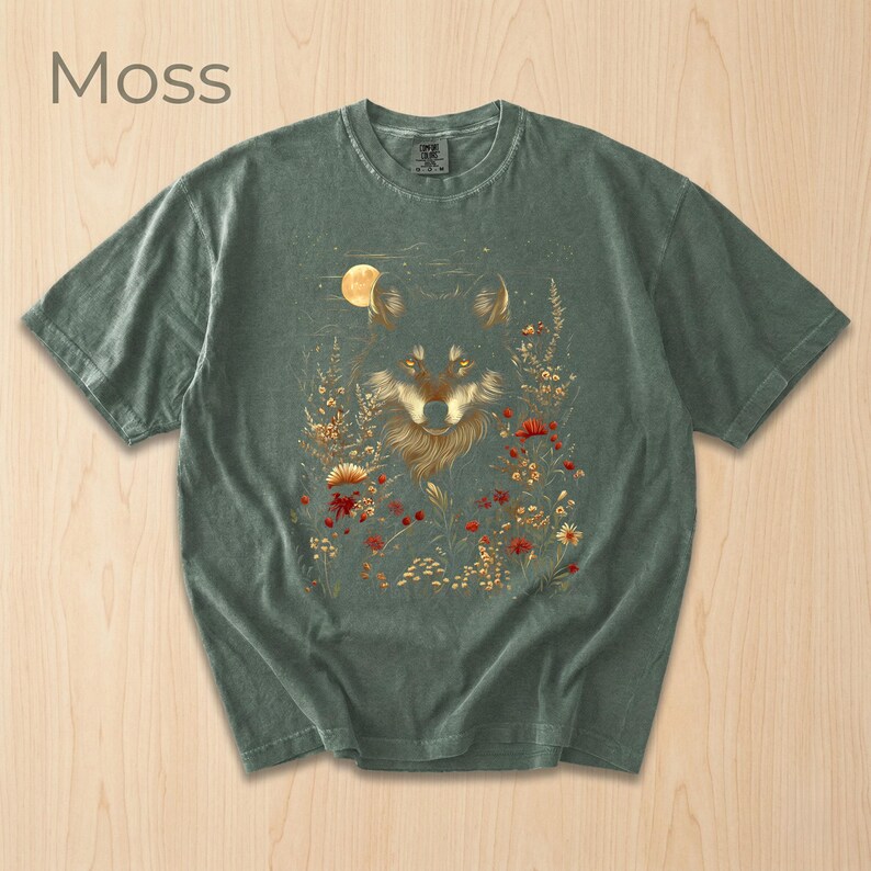 May include: Moss green t-shirt with a wolf illustration amidst flowers and a moon. The wolf has golden fur and intense eyes. The word "Moss" is printed in the upper left corner of the shirt.