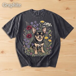 May include: Graphite-colored t-shirt featuring a detailed illustration of a black and tan Chihuahua surrounded by colorful wildflowers. The dog is the focal point, with the text "Graphite" in the upper left corner.