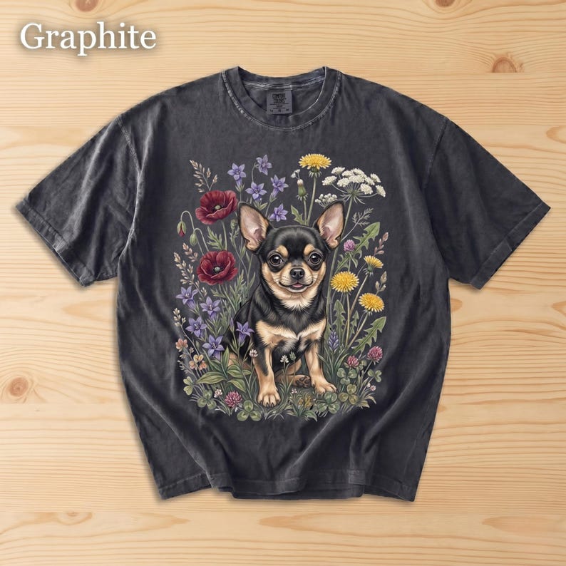 May include: Graphite-colored t-shirt featuring a detailed illustration of a black and tan Chihuahua surrounded by colorful wildflowers. The dog is the focal point, with the text "Graphite" in the upper left corner.
