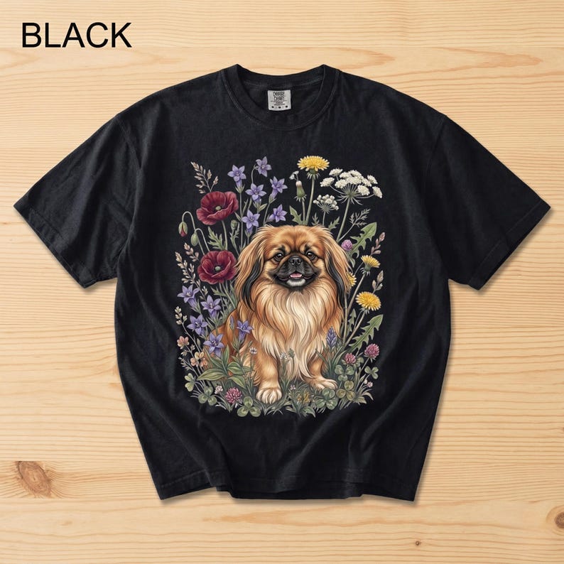 May include: Black t-shirt featuring a detailed illustration of a Pekingese dog surrounded by colorful wildflowers. The dog has long, flowing brown fur and is smiling. The word "BLACK" is printed at the top left.
