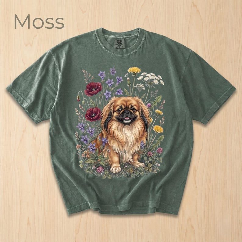 May include: Moss green t-shirt featuring a detailed illustration of a Pekingese dog surrounded by colorful flowers. The dog has long, flowing brown and tan fur. The word "Moss" is printed in the upper left corner.
