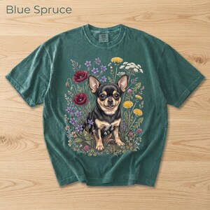 May include: Blue Spruce t-shirt featuring a chihuahua dog illustration surrounded by colorful flowers. The dog is black and tan, with a detailed floral arrangement of red poppies, purple, yellow, and white flowers. The shirt has a vintage, washed look.