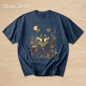 May include: Navy blue t-shirt with a wolf illustration amidst wildflowers and a full moon. The text "Blue Jean" is at the top of the image. The shirt is a relaxed fit, perfect for casual wear.