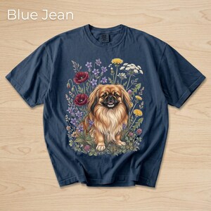 May include: Navy blue t-shirt featuring a detailed illustration of a Pekingese dog surrounded by colorful wildflowers. The text "Blue Jean" is at the top. The dog has long, flowing brown fur and is set against a backdrop of red poppies, purple flowers, and yellow dandelions.