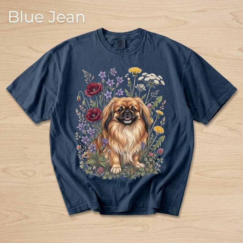 May include: Navy blue t-shirt featuring a detailed illustration of a Pekingese dog surrounded by colorful wildflowers. The text "Blue Jean" is at the top. The dog has long, flowing brown fur and is set against a backdrop of red poppies, purple flowers, and yellow dandelions.