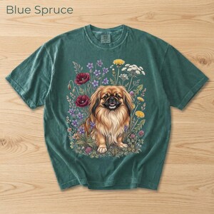 May include: Blue Spruce t-shirt featuring a detailed illustration of a Pekingese dog surrounded by colorful wildflowers. The dog has long, flowing fur and is smiling. The text "Blue Spruce" is at the top left.