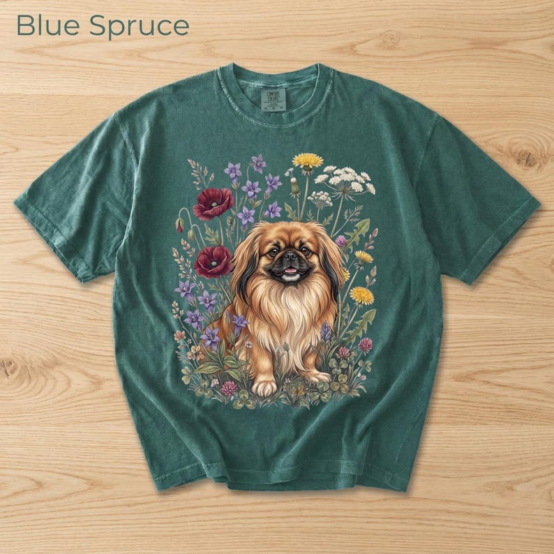 May include: Blue Spruce t-shirt featuring a detailed illustration of a Pekingese dog surrounded by colorful wildflowers. The dog has long, flowing fur and is smiling. The text "Blue Spruce" is at the top left.