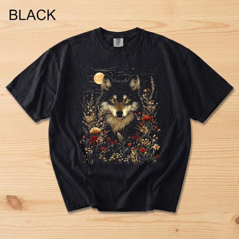 May include: Black t-shirt with a wolf illustration surrounded by flowers and a full moon. The wolf has golden eyes and a light brown chest. The word "BLACK" is printed at the top left of the t-shirt.