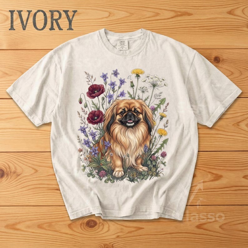May include: Ivory-colored t-shirt featuring a detailed illustration of a Pekingese dog amidst a vibrant floral arrangement. The dog has brown and tan fur, and the flowers include red poppies, purple blooms, and yellow dandelions. The word "IVORY" is printed at the top.