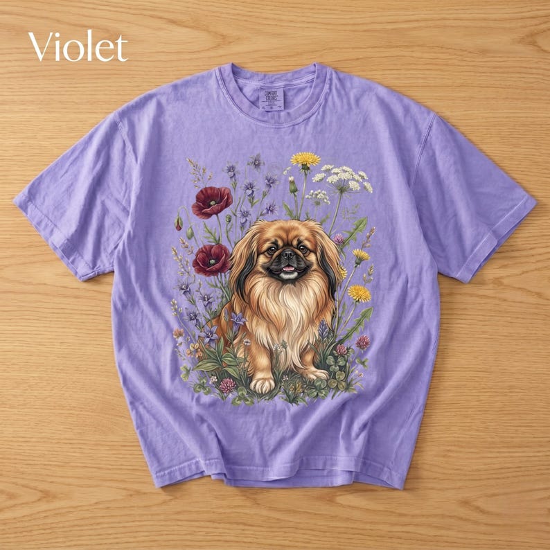 May include: Violet-colored t-shirt featuring a detailed illustration of a Pekingese dog surrounded by wildflowers. The dog has brown and tan fur, and the flowers include red poppies, yellow dandelions, and white blooms. The word "Violet" is printed at the top left.