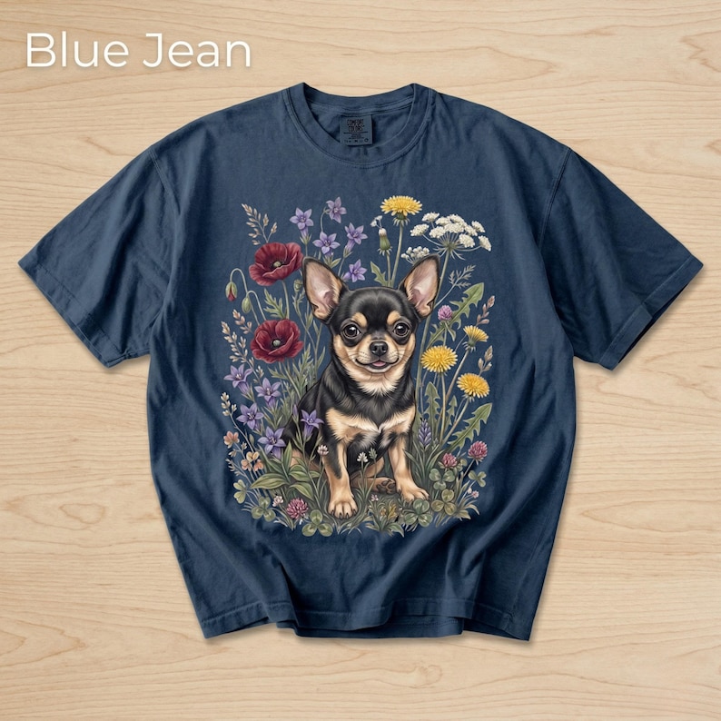 May include: Navy blue t-shirt with a colorful illustration of a Chihuahua surrounded by wildflowers. The text "Blue Jean" is at the top. The graphic features red poppies, yellow dandelions, and purple flowers.