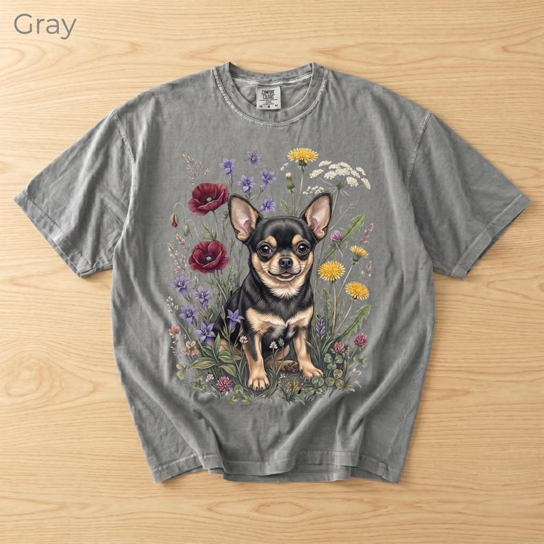 May include: Gray t-shirt featuring a detailed illustration of a Chihuahua dog surrounded by colorful wildflowers. The dog is black and tan, with large ears and a friendly expression. The word "Gray" is printed in the upper left corner.