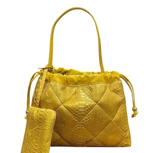 Könnte beinhalten: Eine goldgelbe Handtasche mit einer passenden kleinen Tasche. Die Tasche hat ein gestepptes Rautenmuster und einen Kordelzugverschluss. Sie hat einen einzelnen Griff und besteht aus einem strukturierten Material.