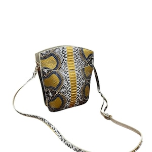 May include: A small handbag with a snakeskin pattern in gold, black, and white. The bag has a long, thin strap and a rectangular shape. The bag is made of a textured material.