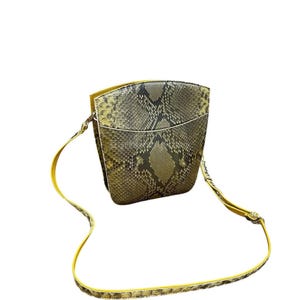 Könnte beinhalten: Eine kleine, strukturierte Umhängetasche mit Schlangenmuster in Grau-, Braun- und Olivgrüntönen. Die Tasche hat einen gelben Riemen und Besatz. Die Tasche ist mit einem Klappenverschluss und einer rechteckigen Form versehen.