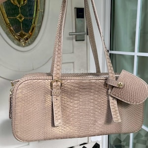 May include: A light brown handbag with a snakeskin pattern. The bag has two handles, a small attached pouch, and a gold-coloured buckle. The bag is rectangular and has a zip closure.