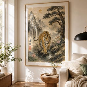 May include: Framed art print featuring a tiger walking towards the viewer in a serene landscape. The artwork showcases a waterfall, lush greenery, and a full moon. The tiger has orange and black stripes. The frame is gold.