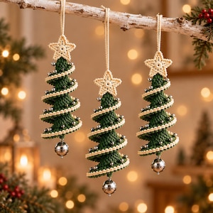 Könnte beinhalten: Drei hängende Weihnachtsbaumschmuckstücke aus dunkelgrünem Häkelgarn. Jeder Baum hat ein spiralförmiges Design mit cremefarbenen Häkelrändern, kleinen silbernen Perlen, einem cremefarbenen Häkelstern an der Spitze und einer silbernen Glocke am Fuß.