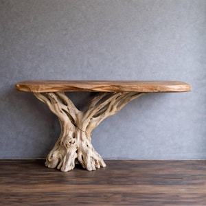 Op de afbeelding: Een unieke houten console met een natuurlijke boomstamvoet die een rechthoekig tafelblad ondersteunt. Het tafelblad is warmbruin, terwijl de voet een lichtere, natuurlijke houtkleur heeft. De tafel is ongeveer 152 cm lang.