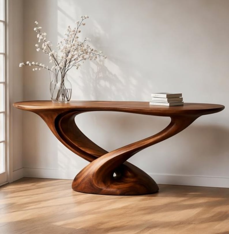 May include: A dark brown, solid wood console table with a distinctive, flowing design. The table has a sculptural base. A glass vase with white flowers and a stack of books are on the table. The table's length is approximately 180 cm.