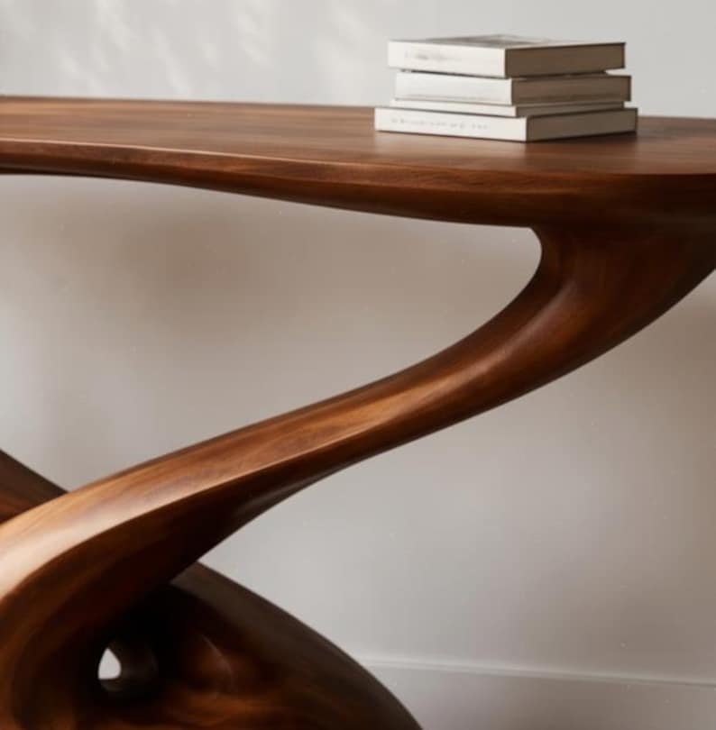 May include: A dark brown wooden console table with a distinctive, flowing design. The table has a smooth, polished finish and a unique, organic shape. Three books with white covers are stacked on the table's surface. The table is a piece of modern furniture.