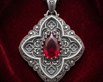 May include: A silver pendant featuring a central pear-shaped deep red gemstone set within an intricate, ornate metal frame with symmetrical scrollwork and quatrefoil cutouts, suspended from a matching silver chain link necklace.