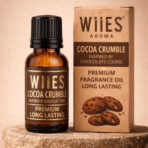 May include: A brown glass bottle and a matching box of "WIIES Aroma Cocoa Crumble" fragrance oil. The bottle and box have gold lettering and a black cap. The box features an illustration of chocolate chip cookies.