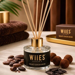 May include: A glass diffuser bottle with a gold cap and reeds. The bottle has a black label with gold text reading "WIIES AROMA VELVET COCOA MUSK." Cocoa beans and chocolate truffles are scattered around the bottle. A box with the same label is in the background.