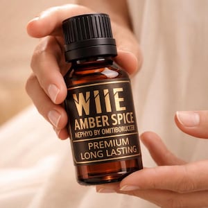 Könnte beinhalten: Eine braune Glasflasche mit schwarzem Deckel, gehalten in den Händen einer Person. Auf dem Etikett steht "WIE AMBER SPICE" in goldfarbenen Buchstaben. Die Flasche ist mit "NEPHYO BY OMITIBORUCCER" und "PREMIUM LONG LASTING" beschriftet.