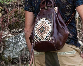 Può includere: Uno zaino in pelle marrone con una patta a motivo geometrico e un pon pon. Lo zaino ha spalline regolabili e una chiusura con cerniera.