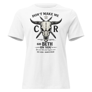 Könnte beinhalten: Weißes T-Shirt mit einem Grafikdesign, das einen Schädel mit Hörnern, gekreuzten Pfeilen und dem Text "DON'T MAKE ME CR GO BETH ON YOU" zeigt. Zusätzlicher Text lautet "You won't like what happens next. EST. 2026 RANCH WEAR."