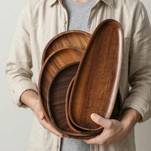 May include: A collection of wooden serving trays in various sizes and shapes. The trays are made of dark brown wood with visible grain patterns. The trays are oval and oblong, perfect for serving appetizers or displaying decorative items.