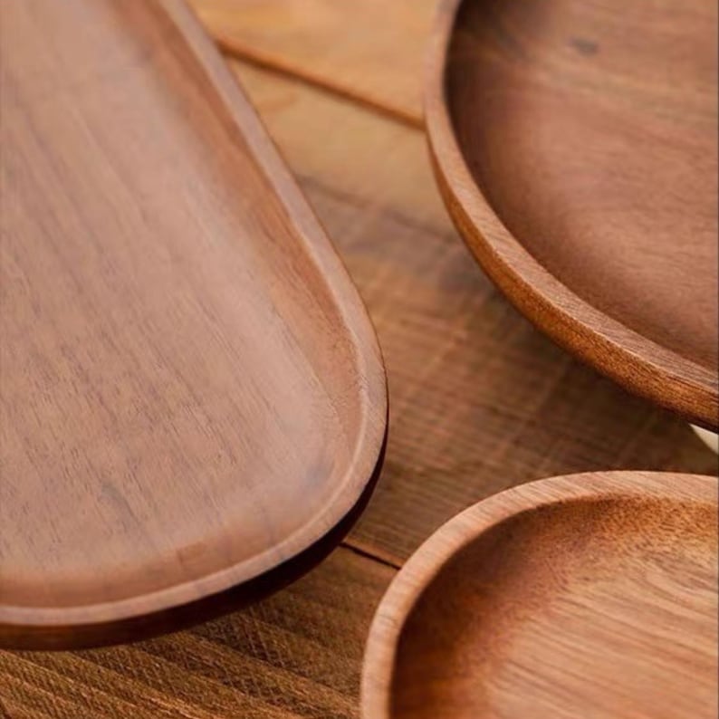 May include: A collection of three smooth, dark brown wooden serving dishes. The set includes one elongated oval tray and two circular bowls, all featuring a natural wood grain pattern and a polished finish with slightly raised, rounded edges.