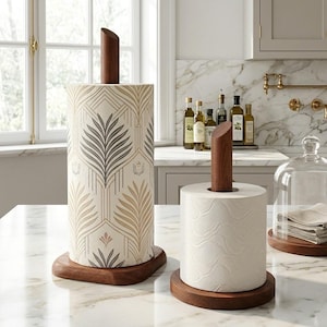 May include: Two wooden paper towel holders. One has a patterned design with beige, brown, and gray leaves. The other holds a roll of white paper towels. Both have a dark brown wooden base and a wooden dowel.