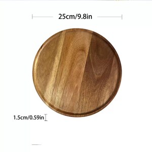 May include: A round wooden serving tray with a natural wood grain finish. The tray is 9.8 inches in diameter and 0.59 inches thick. The tray has a slightly raised edge and is suitable for serving food or displaying items.