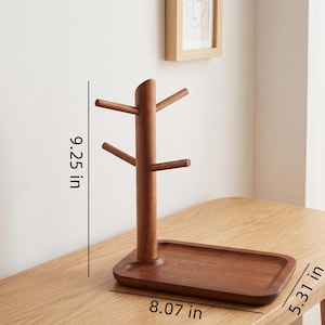 May include: A wooden mug tree with a rectangular base and a tree-like structure for hanging mugs. The mug tree is 9.25 inches tall, 8.07 inches wide, and 5.31 inches deep. The wood has a warm, brown tone.