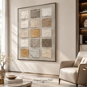 May include: A large rectangular wall art piece featuring a grid of fifteen raised, textured square panels in varying shades of white, beige, tan, gray, and brown, all set within a thin, dark frame against a neutral-colored wall surface.