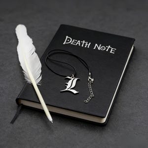 Op de afbeelding: Een zwart notitieboek met de woorden "Death Note" in witte letters, een zilveren hangerketting met de letter "L" en een witte veerkiel. Het notitieboek is gesloten en heeft een zwart lint als bladwijzer.