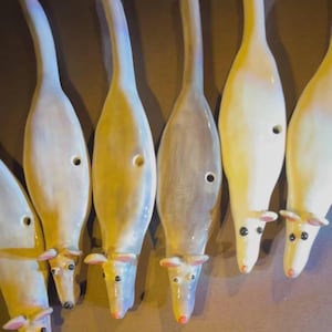 Könnte beinhalten: Eine Sammlung von pfeifenden Ratten aus Keramik. Jede Pfeife ist in Weiß-, Creme- und Grautönen bemalt, mit einem kleinen Loch und einer rosa Nase. Die Pfeifen sind in einer Reihe angeordnet und zeigen ihr einzigartiges Design.