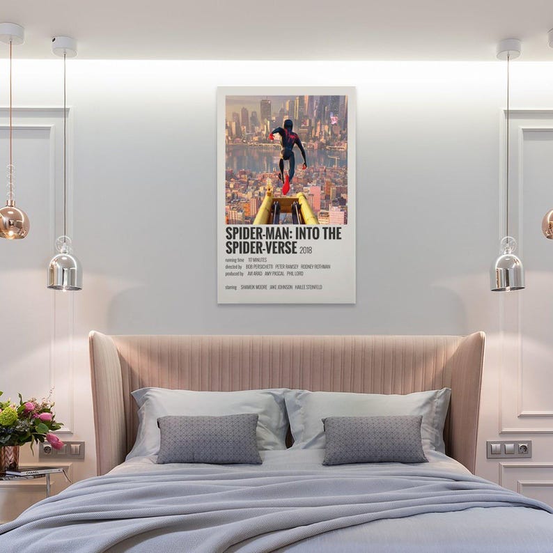 May include: A framed movie poster for "Spider-Man: Into the Spider-Verse" (2018) hangs above a bed. The poster features Spider-Man in a dynamic pose against a cityscape backdrop. The bed has a pink headboard, gray pillows, and a light blue blanket.