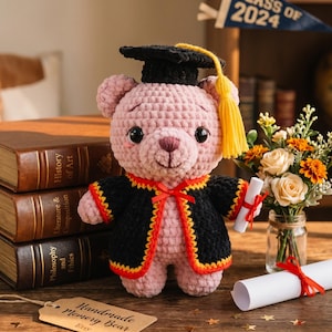 May include: A handmade pink crochet bear wearing a black graduation cap and gown with a yellow tassel. The bear holds a diploma tied with a red ribbon. A banner reads "Class of 2024."