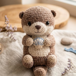 Può includere: Un peluche di lontra fatto a mano all'uncinetto, nei toni del marrone e del crema, che tiene una conchiglia blu e bianca. La lontra ha una testa rotonda, piccole orecchie e un'espressione dolce. Un oggetto artigianale affascinante.