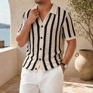 May include: A short-sleeved, button-down shirt with vertical black stripes on an off-white background. The shirt has a collared neckline and is paired with white pants. The style is casual and suitable for warm weather.