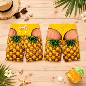 Op de afbeelding: Een zwembroek met een realistische ananasprint en een grafisch ontwerp van huidkleurige billen die een gele string of bikinibroekje dragen. De short heeft een wit trekkoord in de taille en groene accenten van ananasbladeren.