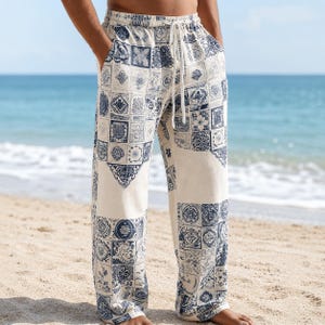 May include: Loose-fitting trousers featuring a cream base color with a repeating navy blue tile-inspired pattern. The pants include an elastic waistband with a white drawstring cord and two side pockets, extending down to the ankles.
