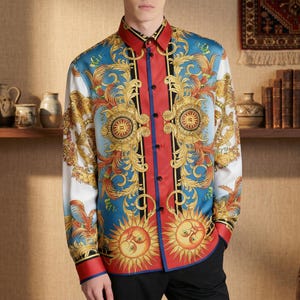 Op de afbeelding: Een overhemd met lange mouwen en een opvallend barokontwerp. Het overhemd heeft een rode kraag en sluiting, met een blauw-witte achtergrond versierd met gouden krullen en zonmotieven. De manchetten zijn rood met blauwe bies.